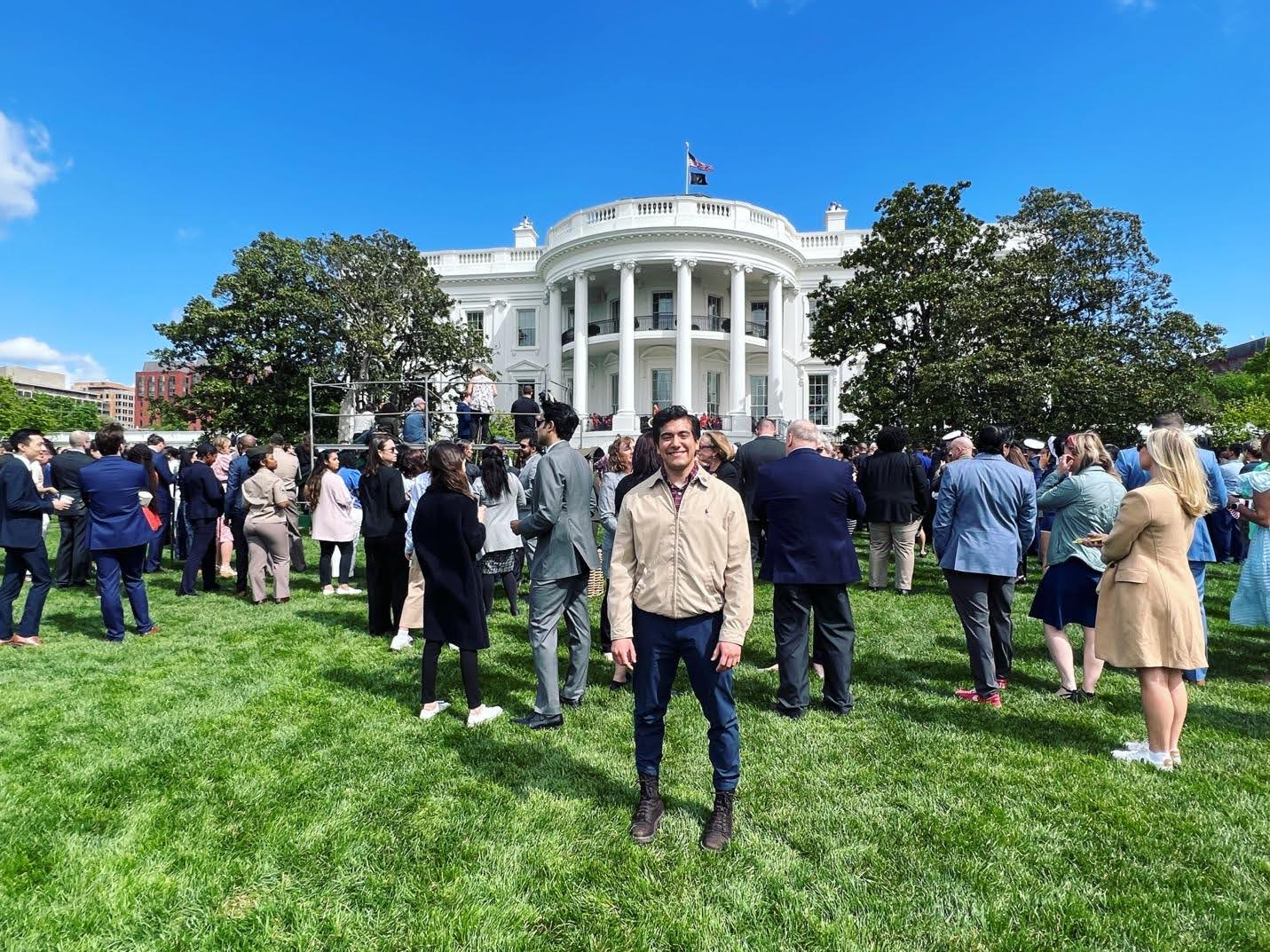 A person smiling in the foreground at a crowded event on the lawn of the White House.