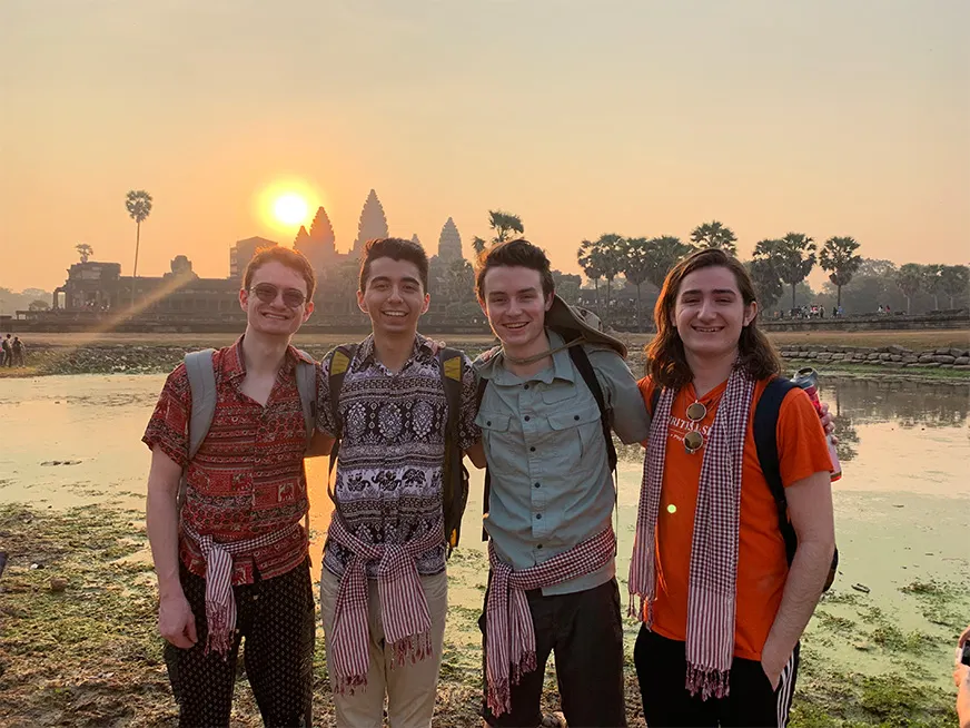 Four students smiling. Behind them a lake, and a temple.