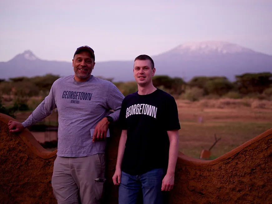 A student and a professor smiling, behind them a mountain