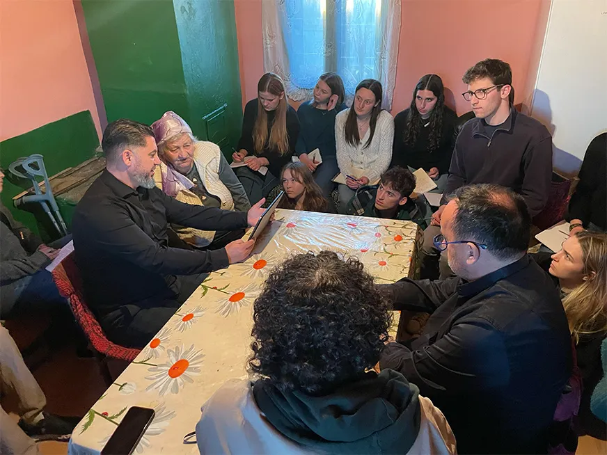 Group of students sitting around a table looking at two adults that are holding an iPad, in Romania