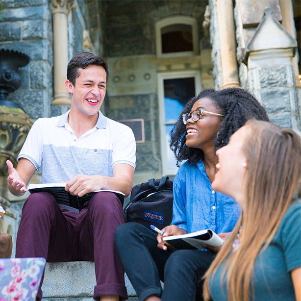 Five students sitting on Healy steps, laughing with books on their laps.