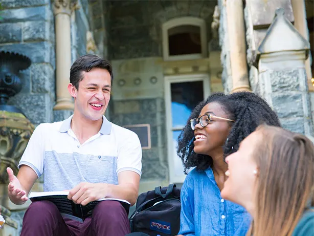 Five students sitting on Healy steps, laughing with books on their laps.