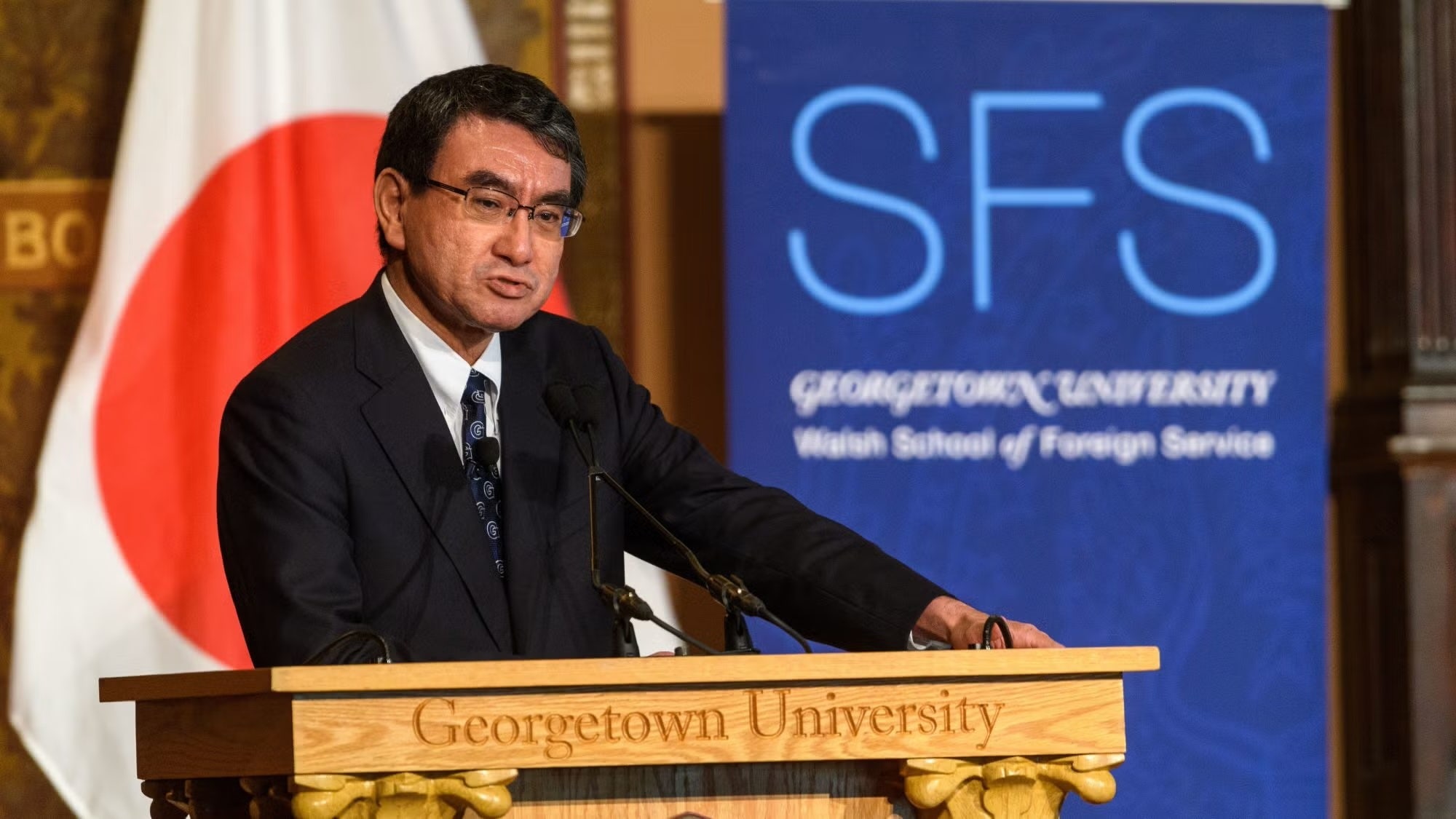 Kono Taro speaks from podium engraved with words "Georgetown University." An SFS banner and Japanese flag are in the background.