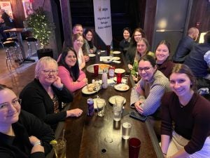 Group of people smiling at a table in a pub. Drinks and food are visible on the table.