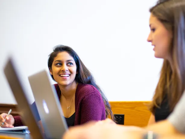 students in class talking with each other while taking notes.
