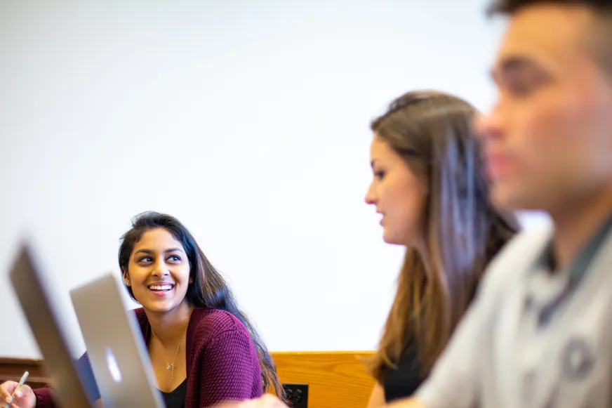 Students in class talking with each other while taking notes.