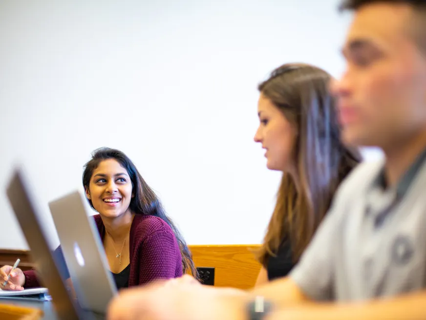 students in class talking with each other while taking notes.