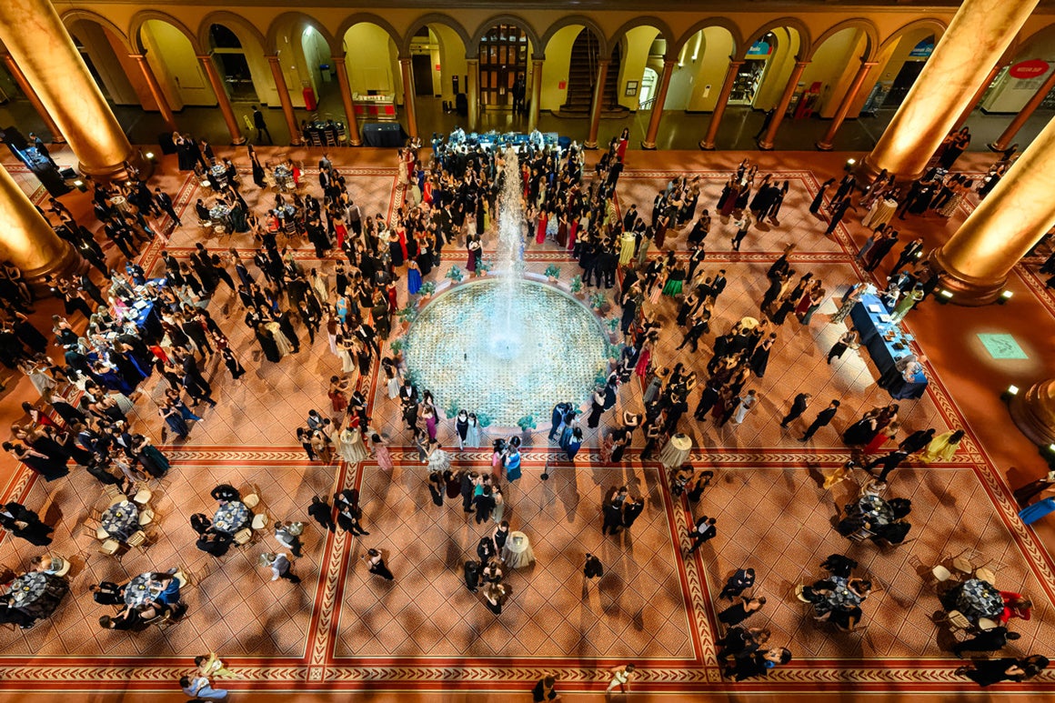 Aerial view of the National Building Museum at night. A large crowd of people are spread across the venue wearing gala attire, featured in the middle a water fountain.