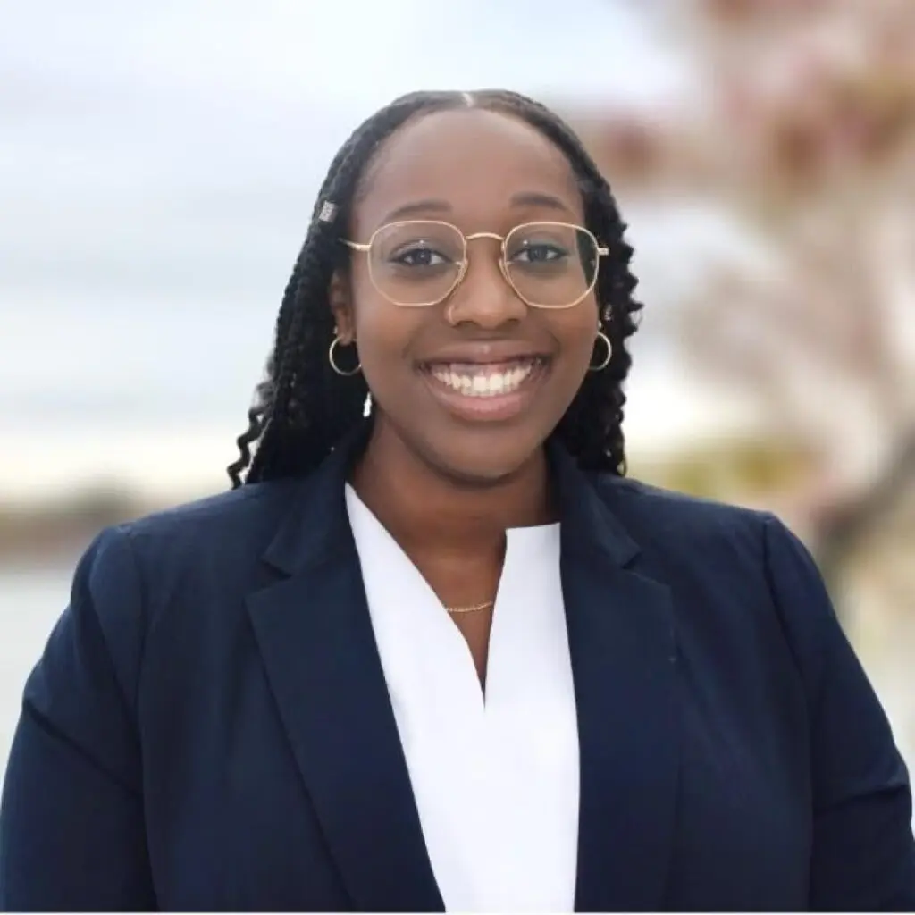 Adia Armstrong wearing a navy blue blazer, a white blouse and glasses.
