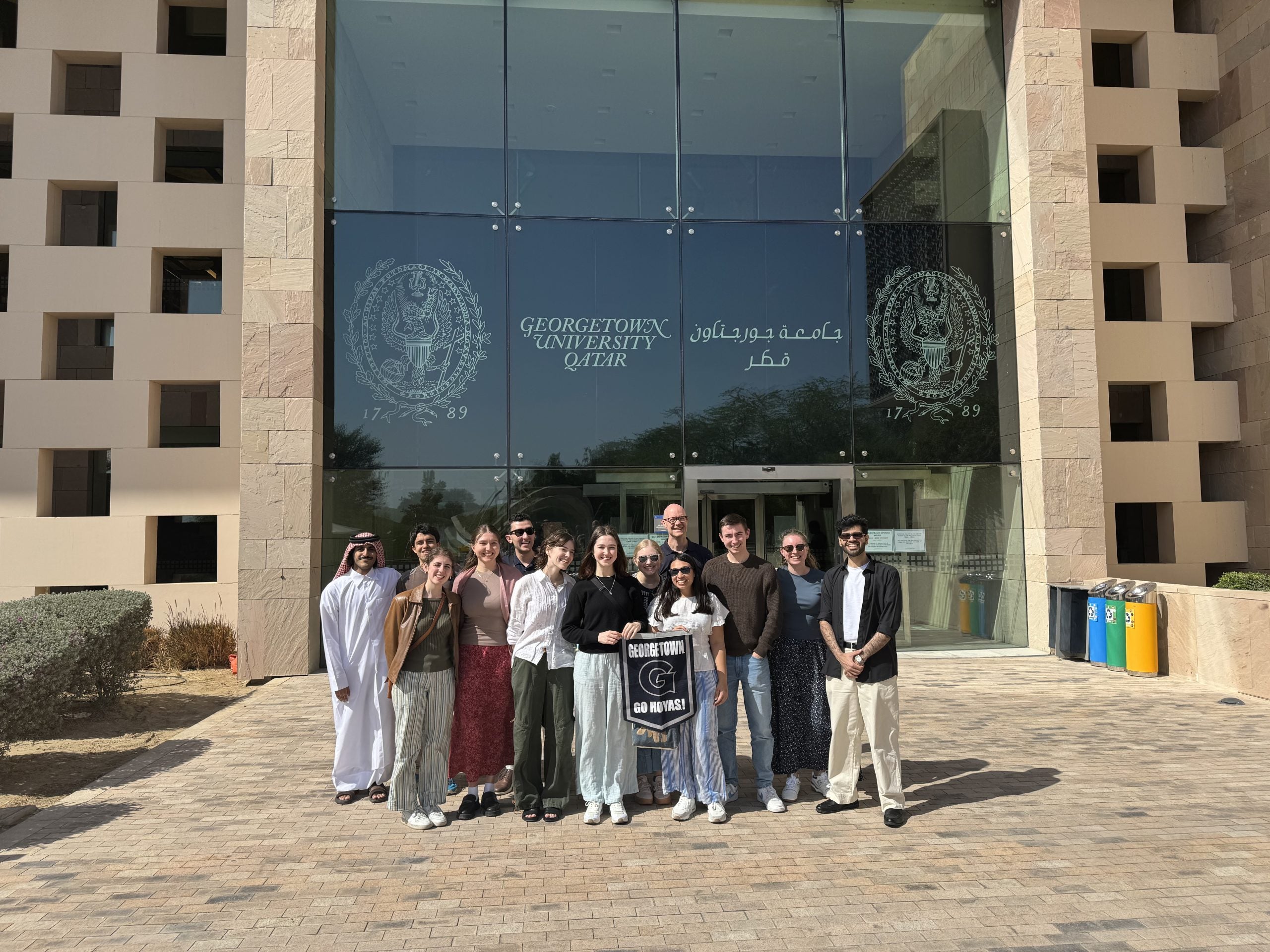 A group of college students standing in front of Georgetown University in Qatar's building, smiling for a photo.