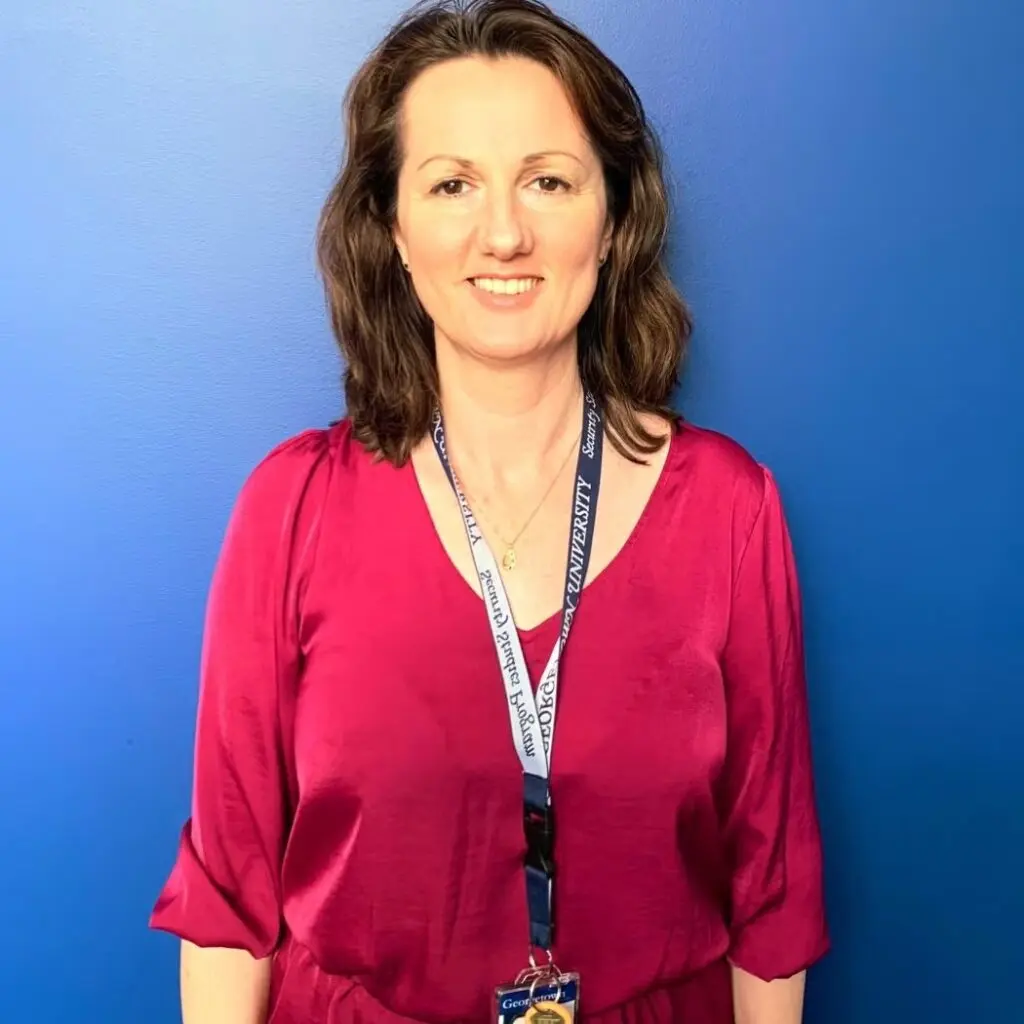 Alzbeta Findlay wearing a magenta shirt, a lanyard and standing against the blue background.
