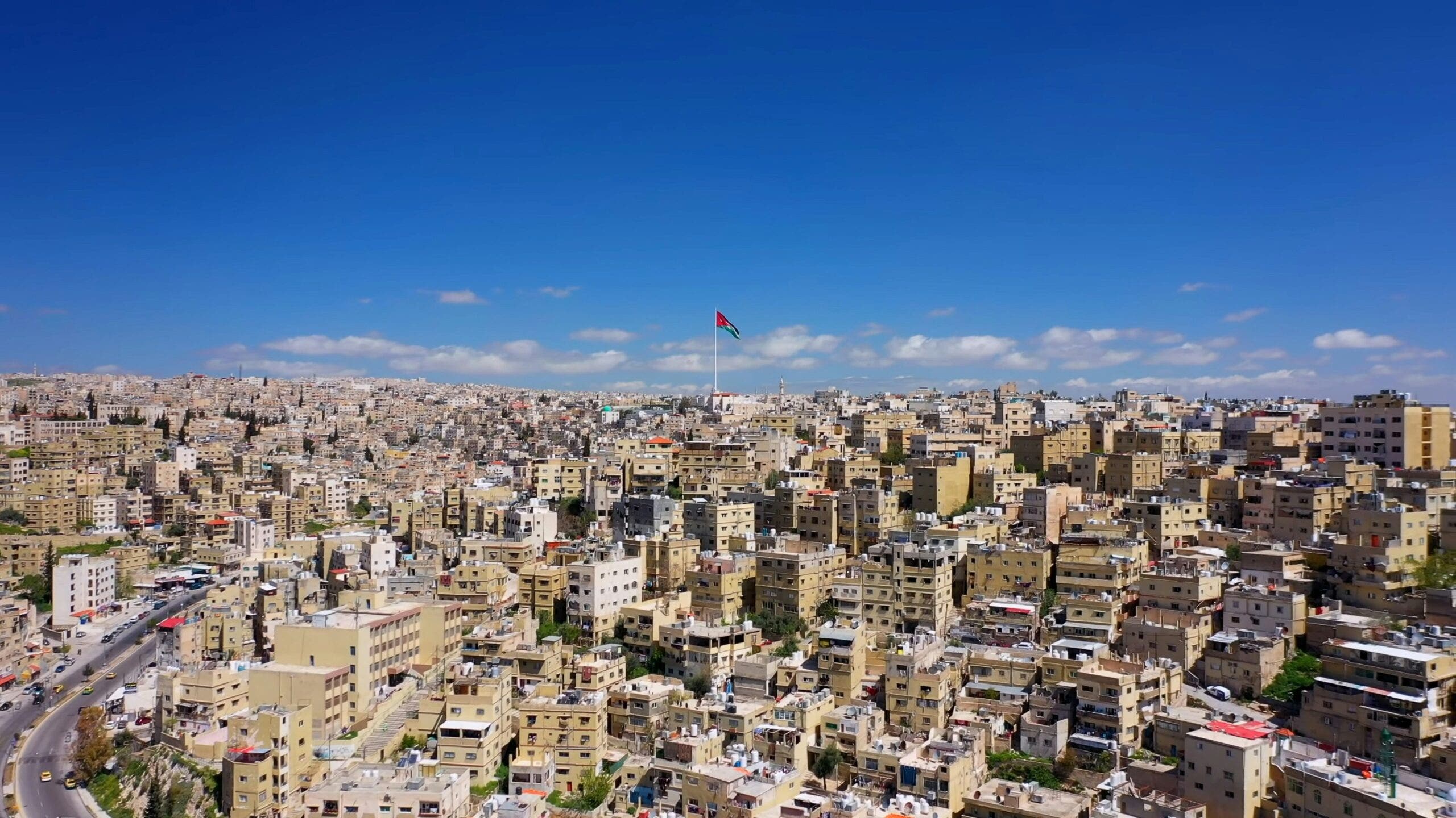 Aerial view of Amman, Jordan, showcasing densely packed buildings and a large flagpole with the Jordanian flag in the center.