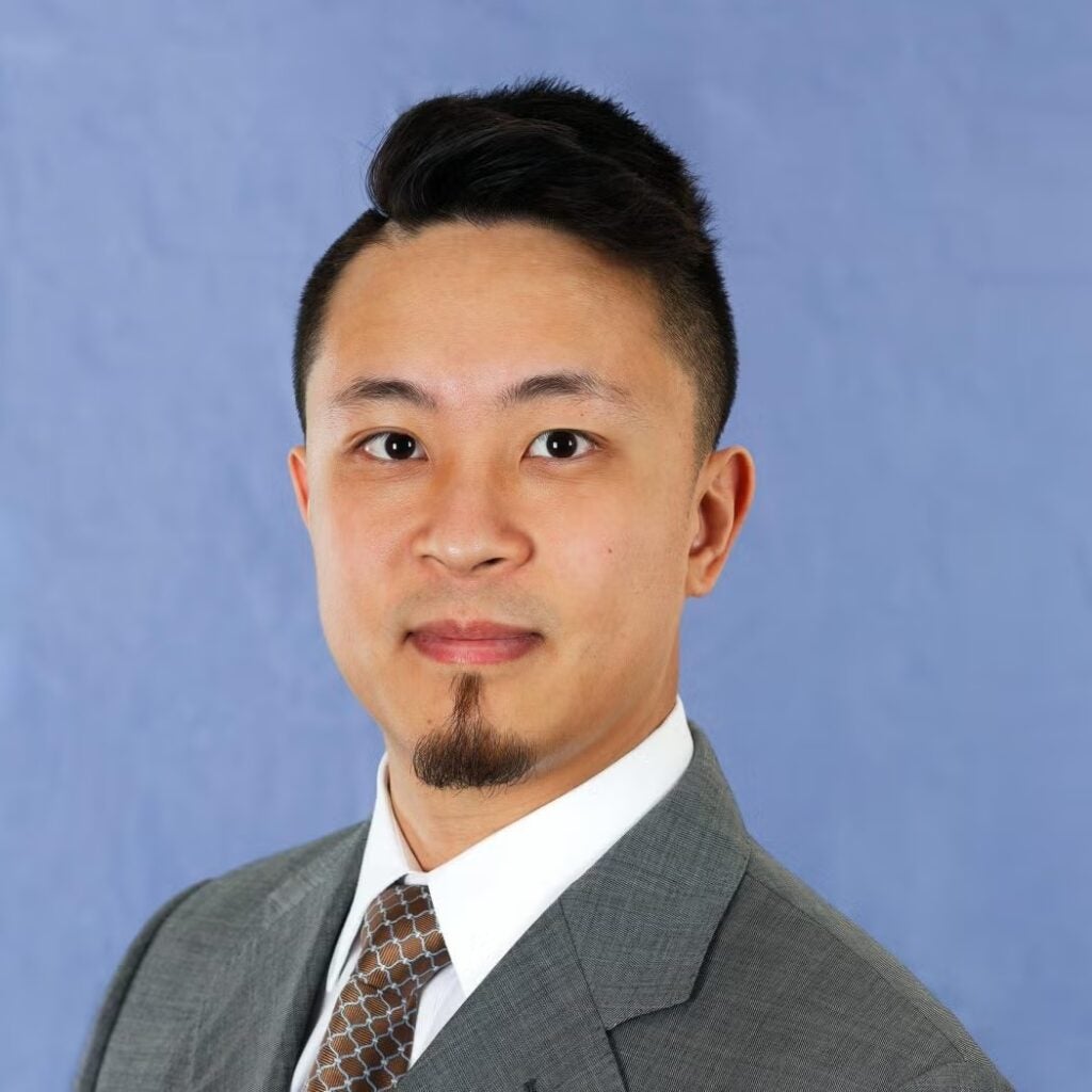 Andrew Yang wearing a gray suit, brown tie and white button-down shirt.