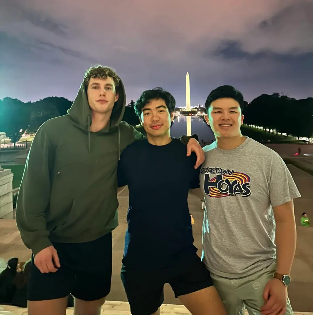 Andrew Park stands with two friends in athletic attire on the National Mall at night.