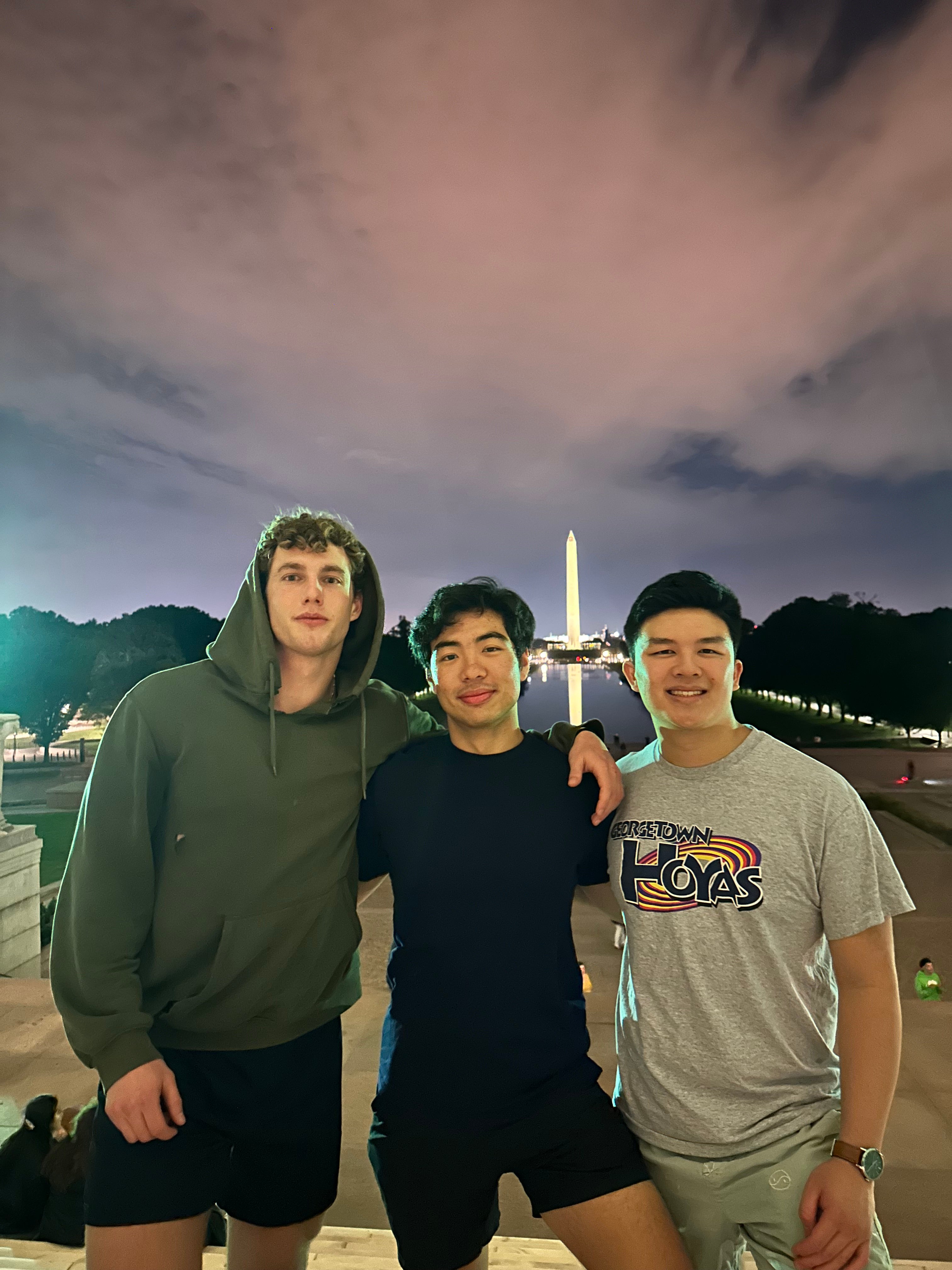 Andrew Park stands with two friends in athletic attire on the National Mall at night.