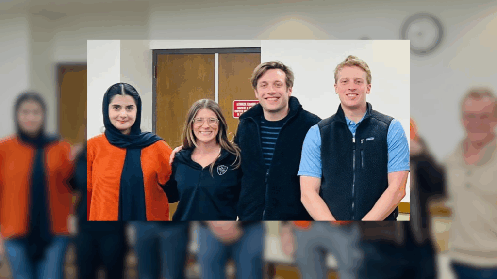 Group photo of seven individuals smiling in an indoor setting with a clock on the wall.