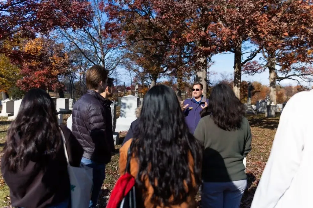 A group of people listening to a tour guide at Arlington National Cemetery during autumn.