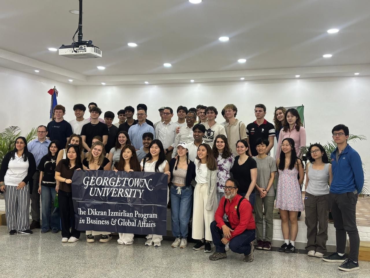 Large group of college students stand holding a banner that says Georgetown University standing in an open office lobby.