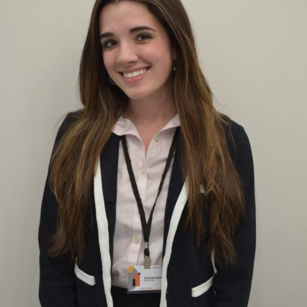 Bethe Bogrette wearing a black and white blazer, a white button-down shirt and a conference lanyard.