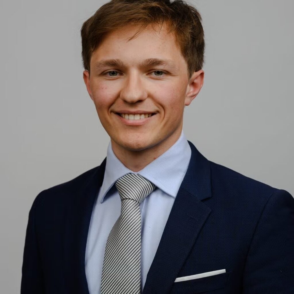 Blaise Hanson wearing a navy blue blazer, a striped tie and a light blue shirt.