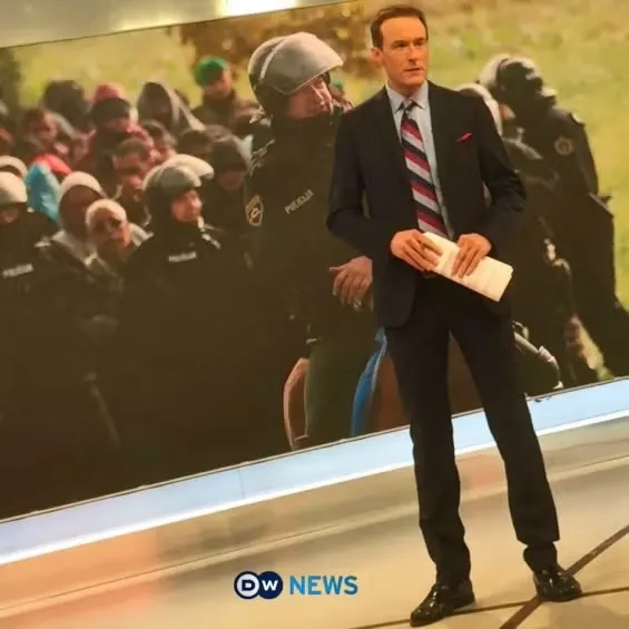 Brent Goff, MAES alumni, standing in suit and tie preparing to read the news.