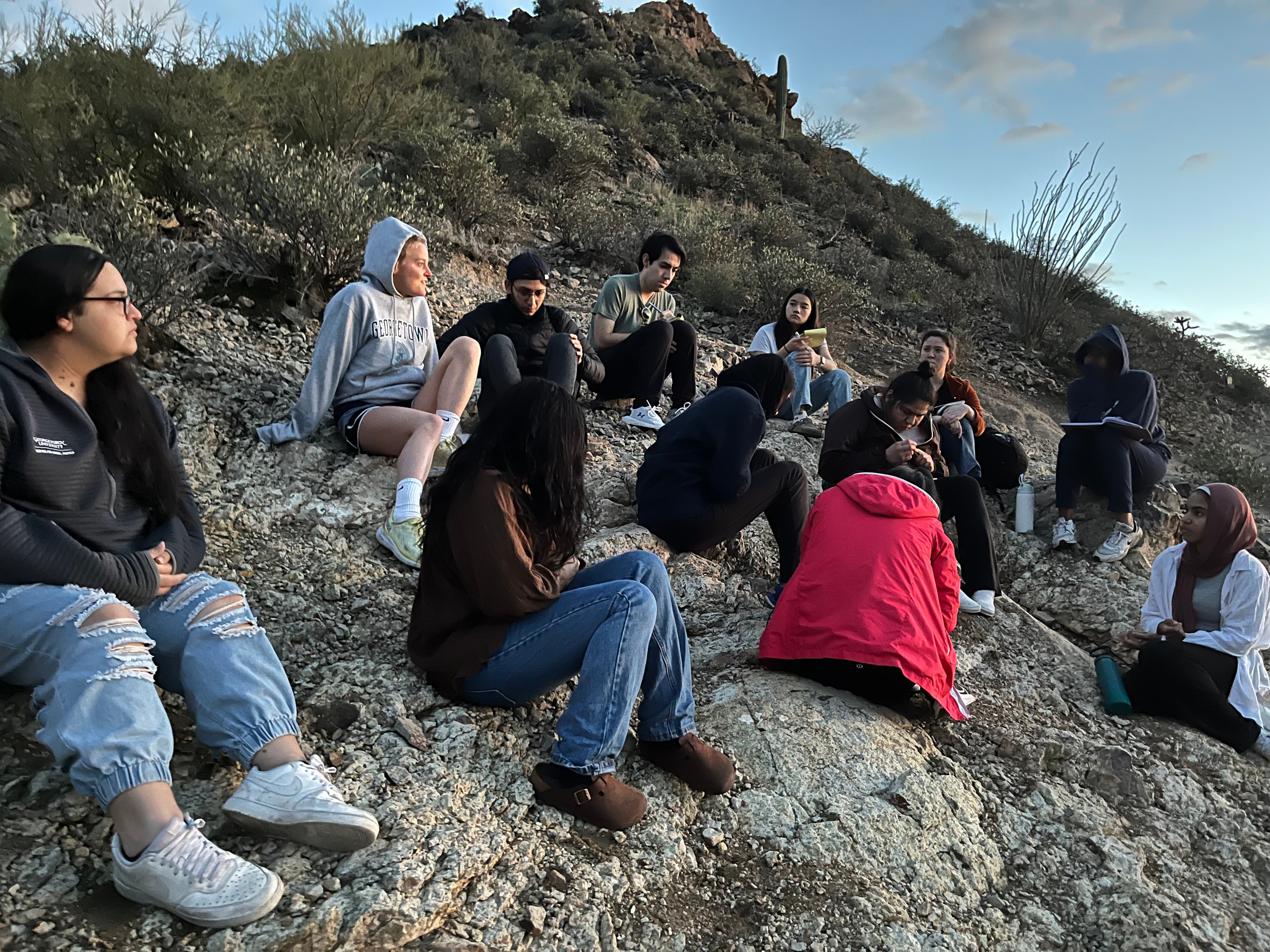 Bolaños and classmates sit on a hill covered in rocks and brush at the U.S.-Mexico border.