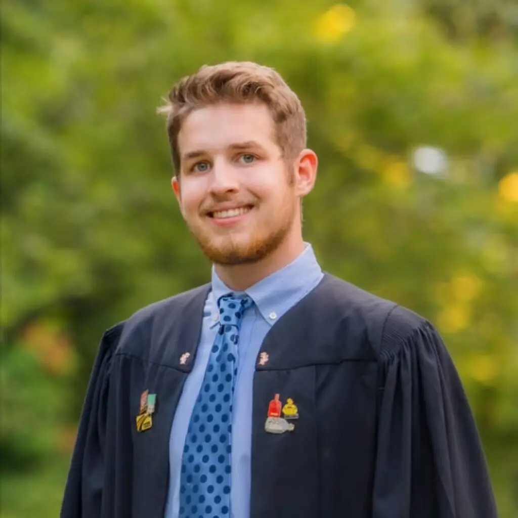 Cam Williams wearing graduation regalia, a light blue, button-down shirt, and a blue polkadot tie.