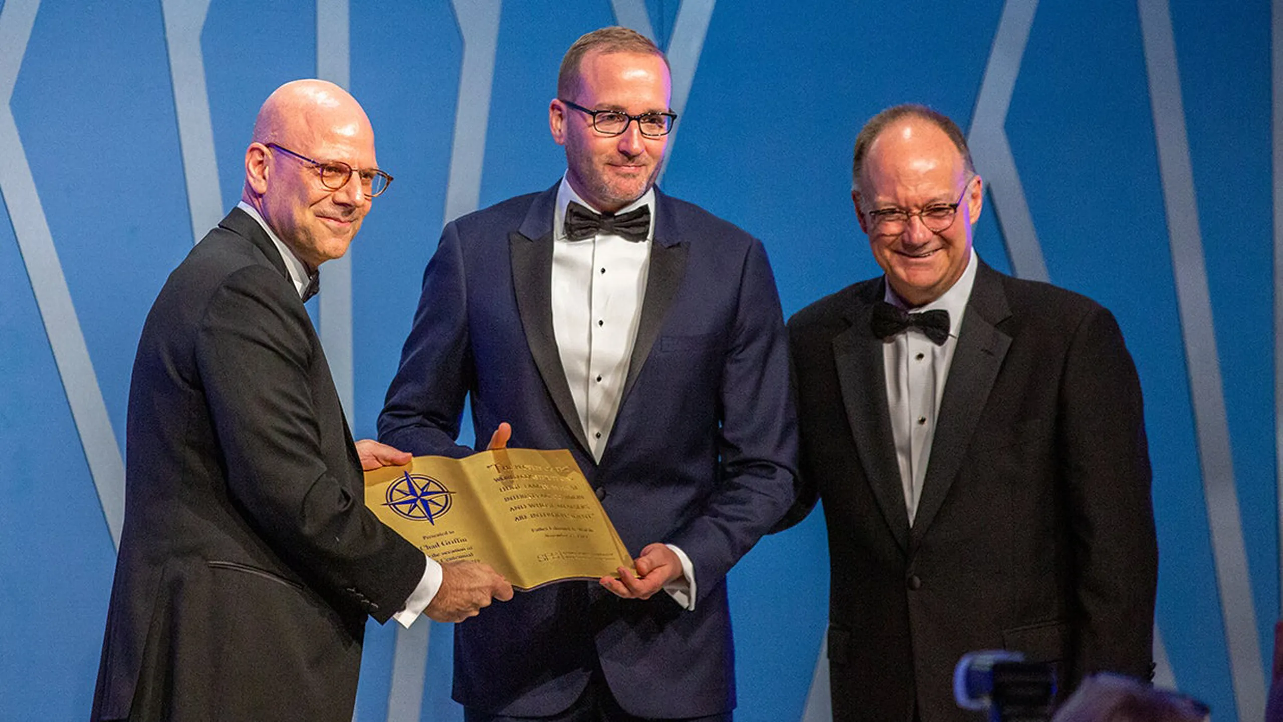 President John J. DeGioia and SFS Dean Joel Hellman presenting the Centennial Honors award to Chad Griffin. All three men wearing formal attire.
