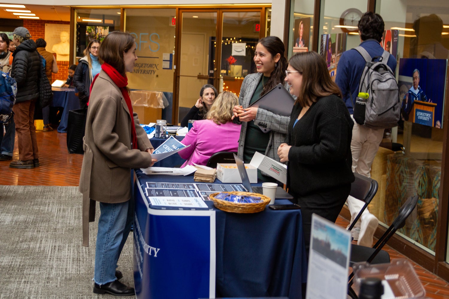 certificate fair in the Intercultural Center. Student is speaking to two staff members while holding a pamphlet. between them a table with papers and doughnuts