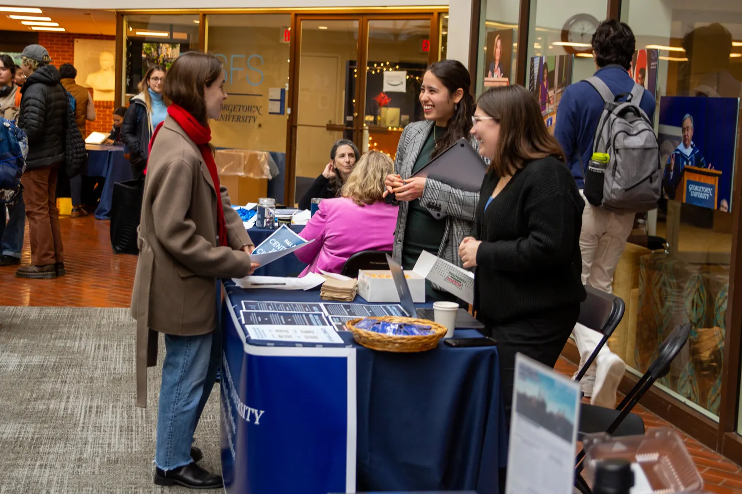 certificate fair in the Intercultural Center. Student is speaking to two staff members while holding a pamphlet. between them a table with papers and doughnuts