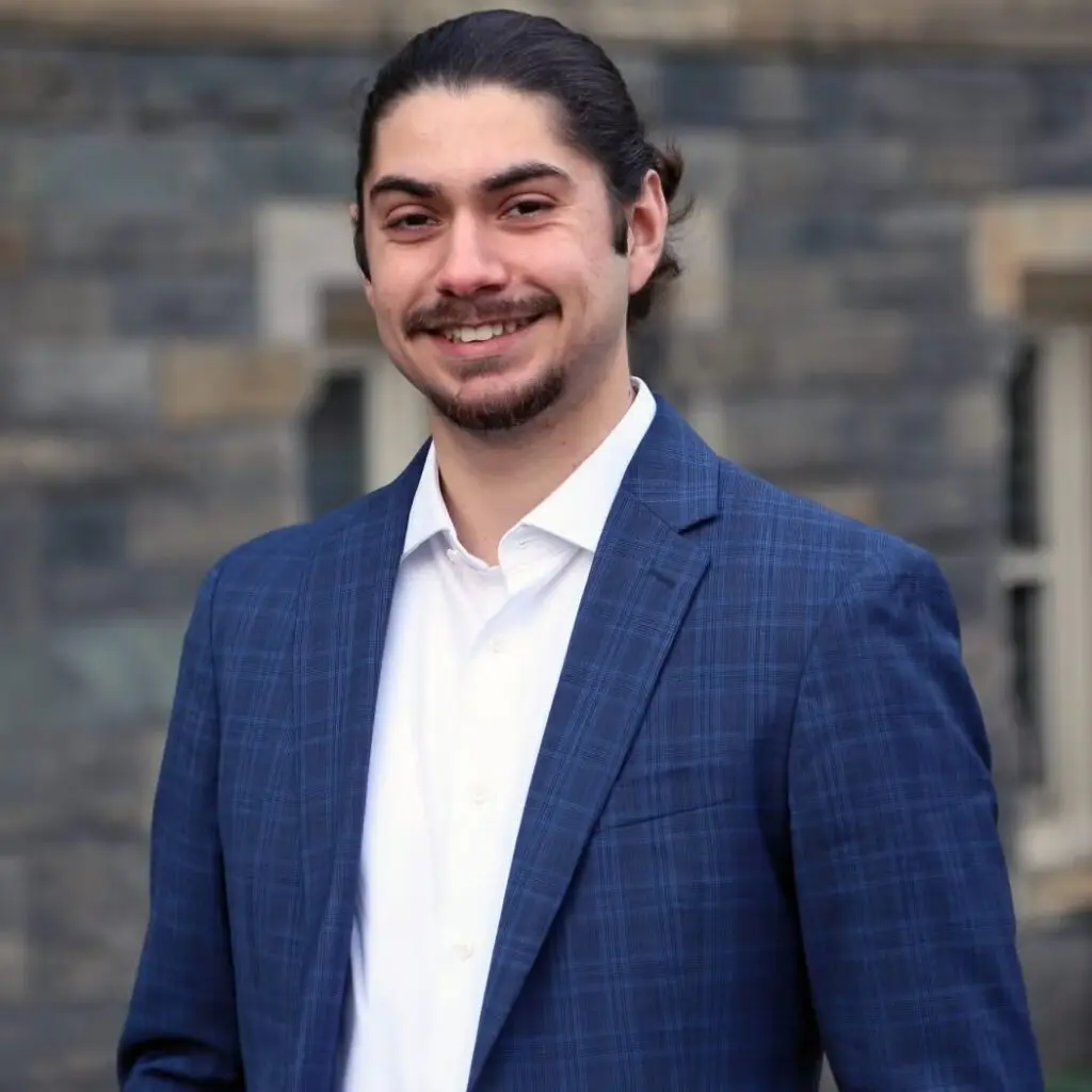 Christian Soenen wearing a blue plaid blazer and a white button down shirt and smiling.