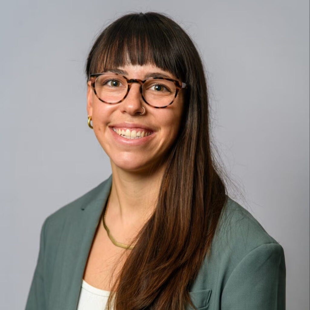 Claudia Gonzalez wearing a grey blazer and glasses, and smiling.