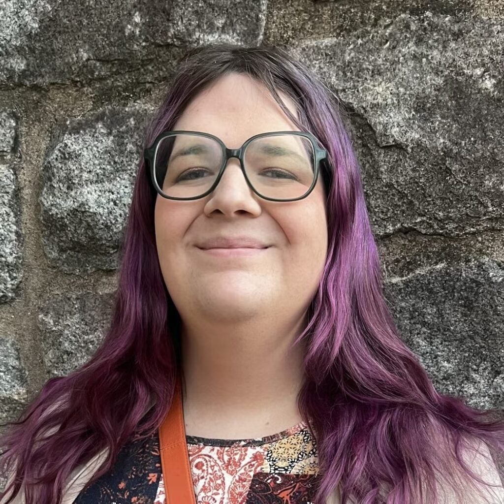 Coco Tait wearing a multicolor, paisley blouse and glasses.