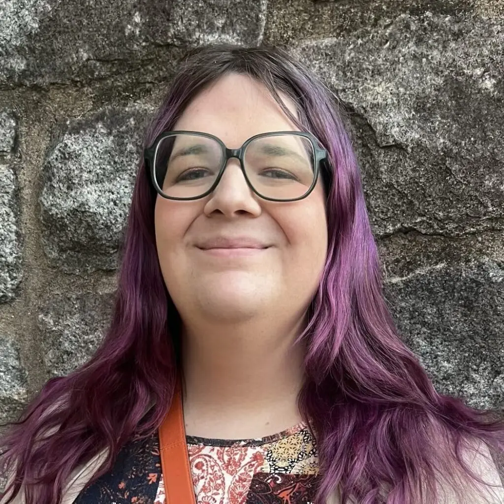 Coco Tait wearing a multicolor, paisley blouse and glasses.