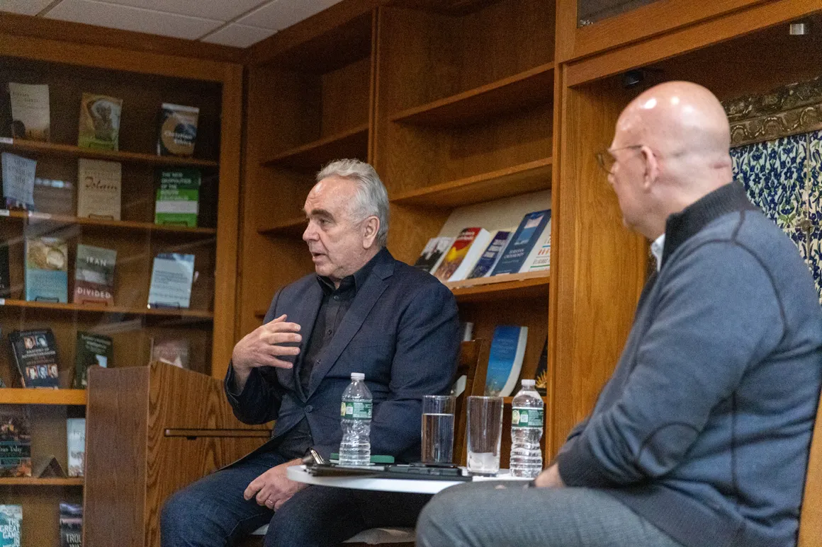 Dean Hellman sitting opposite to Kurt Campbell, engaged in conversation. Behind them book shelves filled with books.