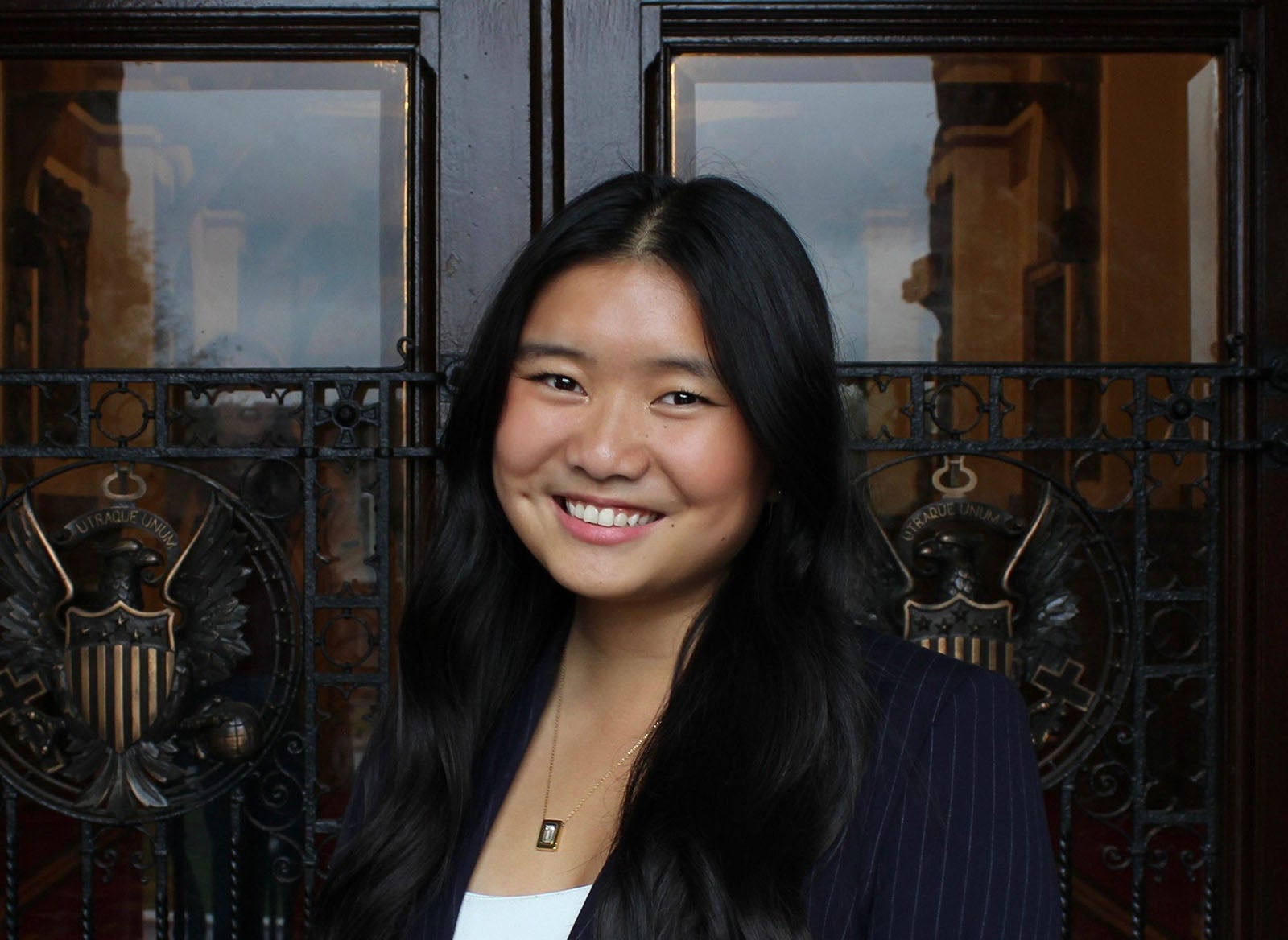 A young woman with long black hair wearing a pinstriped suit and a white shirt.