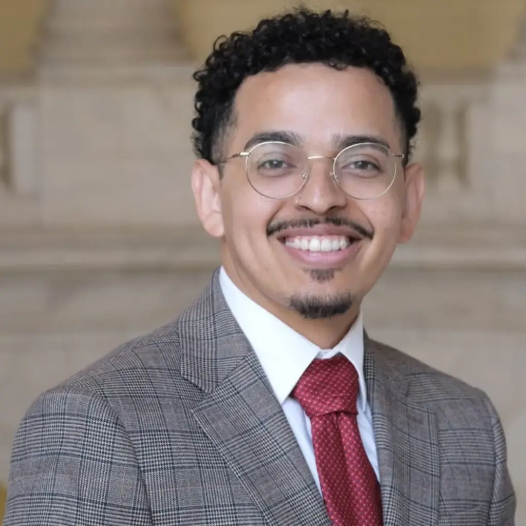 Daniel Castro Bonilla wearing a gray plaid suit, a red tie, a white button-down shirt with glasses