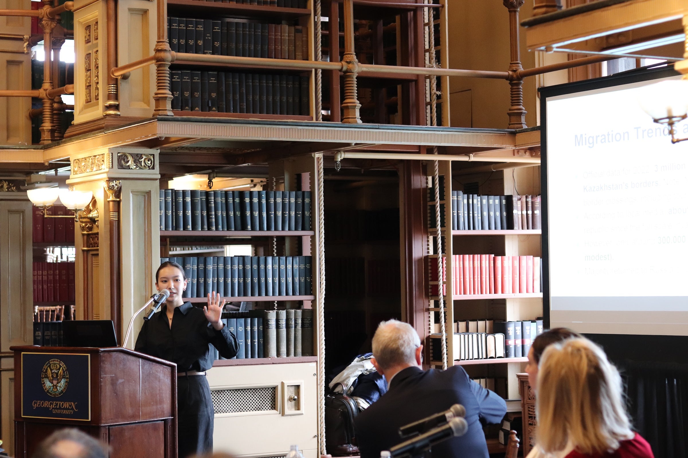 Darina Zhunussova stands at the pidum in Riggs Library presenting to an audience.