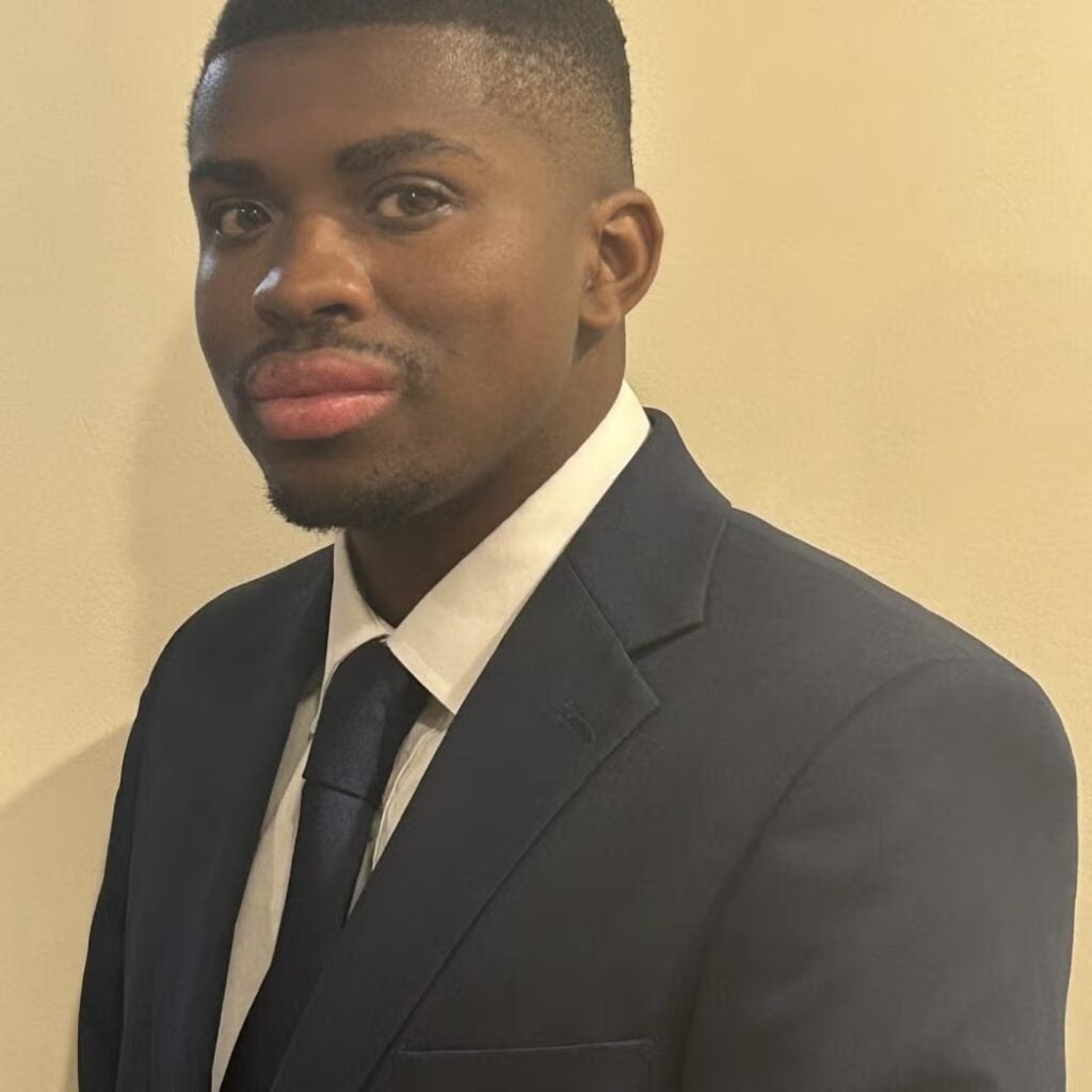 Deontae Brown wearing a black blazer, a white button-down shirt with a navy blue tie.