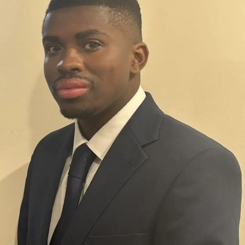 Deontae Brown wearing a black blazer, a white button-down shirt with a navy blue tie.