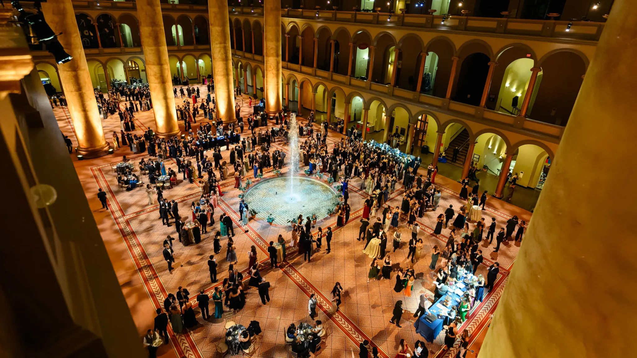 Aerial view of the National Building Museum at night. A large crowd of people are spread across the venue wearing gala attire, featured in the middle a water fountain.