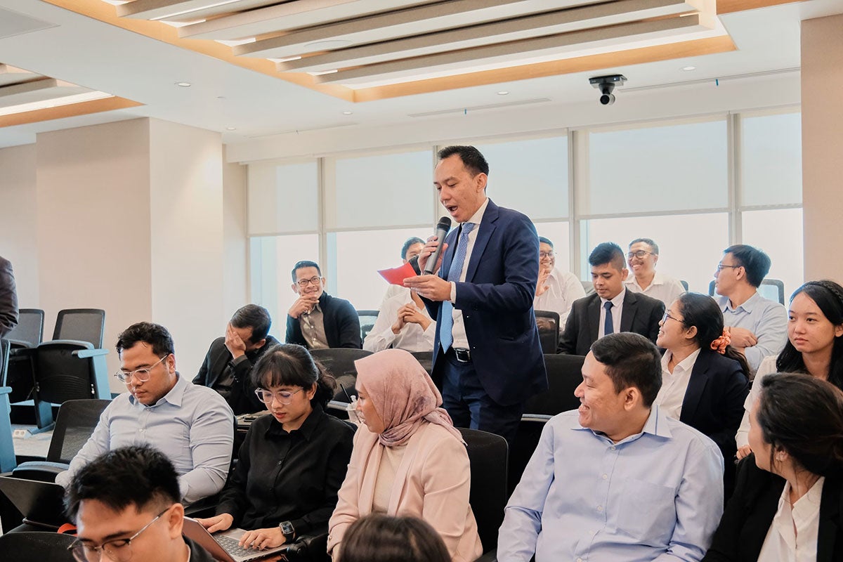 A large group of college students in theatre style seating listen to an instructor in a navy suit speak into a microphone.