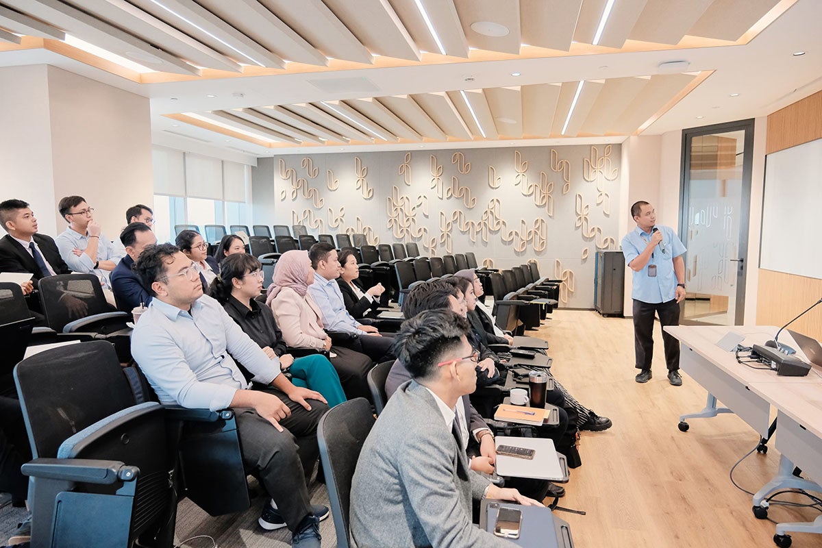 Sixteen college students sit in theatre style seating looking at a white board. Instructor in light blue shirt speaks into a microphone.