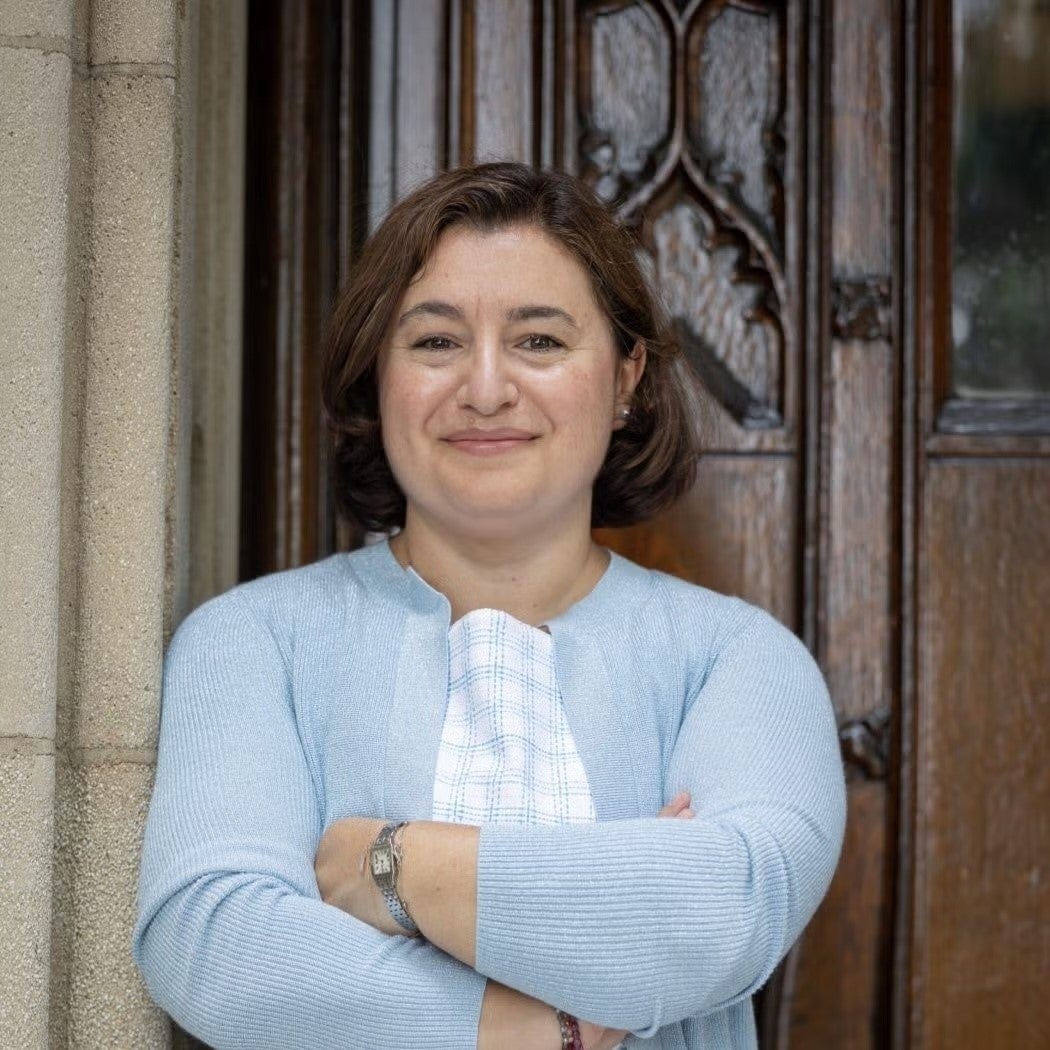 A headshot of Ekin Birol standing in front of a wooden door, wearing a light blue sweater.