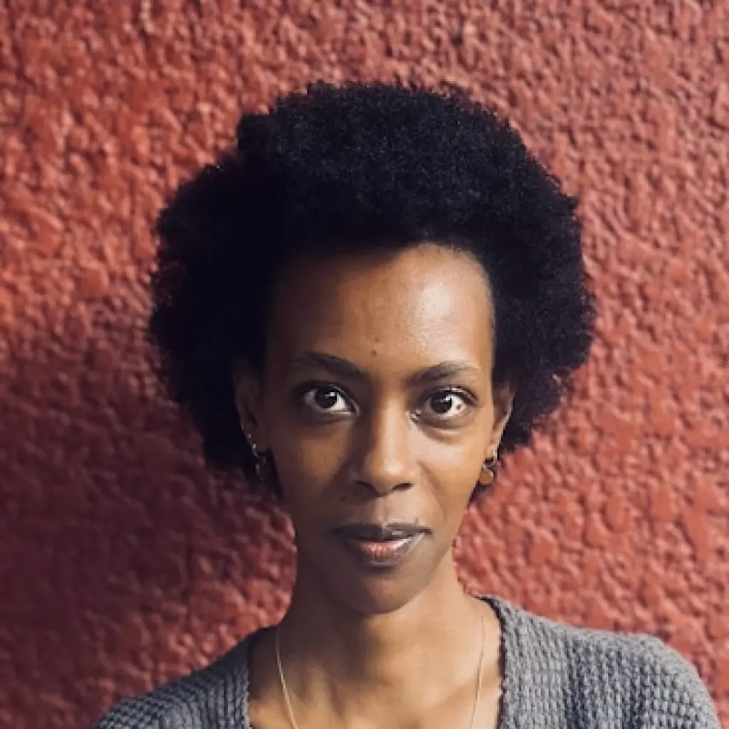 Elizabeth Umutesi Queen wearing a gray shirt against a red background.