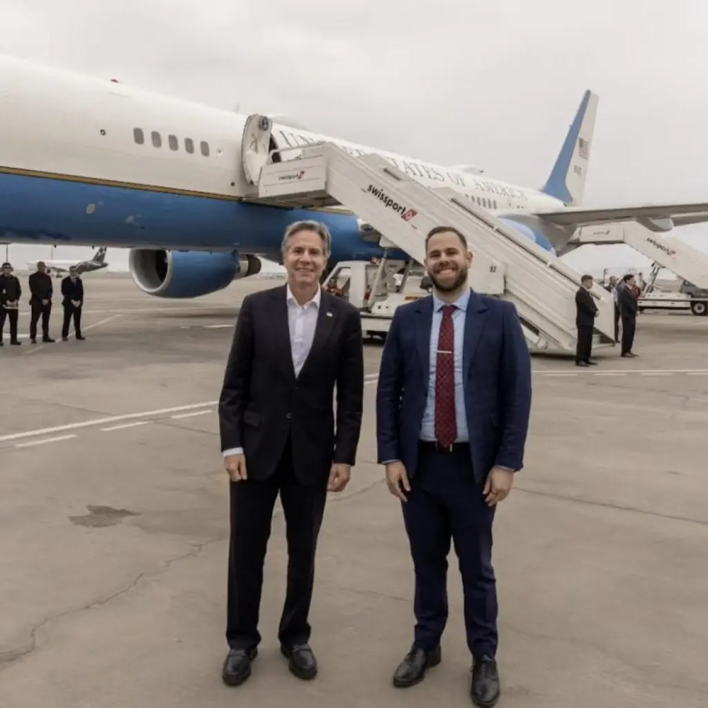 Two men in suits in front of an airplane on a tarmac.