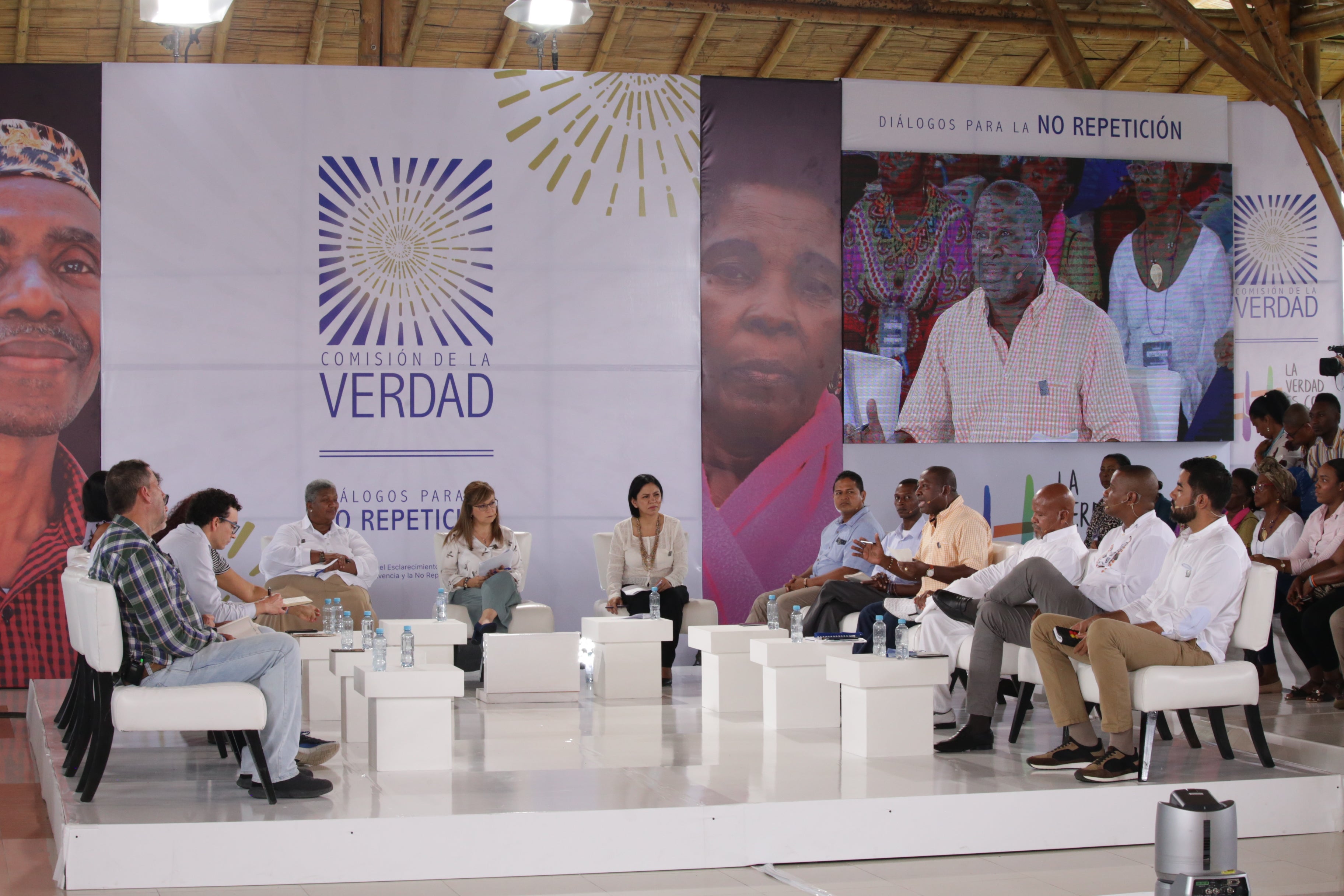A large group of people sitting on a white stage with a backdrop that says "Comision de la Verdad."