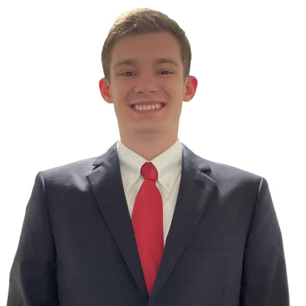 Evan McDonnell wearing a dark blazer and white button-down shirt with a red tie.