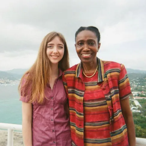 Fiona Naughton next to woman, both smiling. Behind them the view of an ocean, mountains and greenery, on a cloudy day.