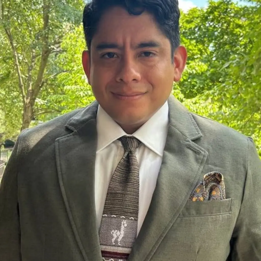 Gabriel McKern wearing a sage green blazer, a white button-down shirt and a tie with a llama on it.